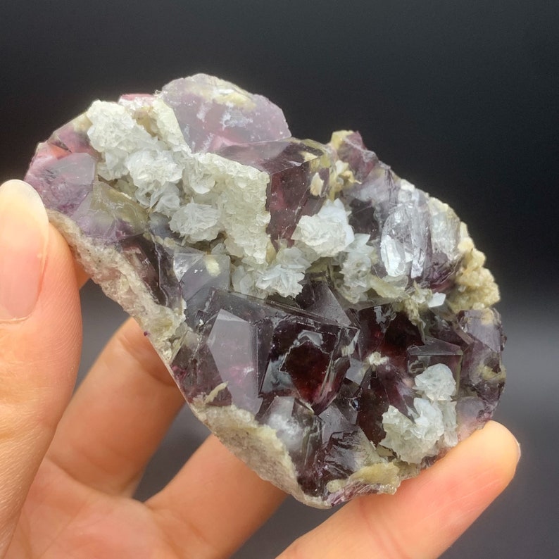 May include: A cluster of purple and green fluorite crystals with white calcite crystals. The fluorite crystals are translucent and have a glassy lustre. The calcite crystals are opaque and have a dull lustre.