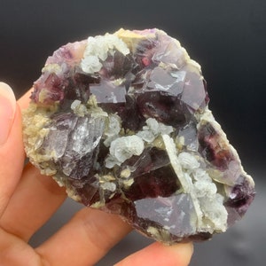 May include: A cluster of purple fluorite crystals with a light purple hue and a few white calcite crystals. The fluorite crystals have a cubic shape and are translucent. The calcite crystals are smaller and more opaque.