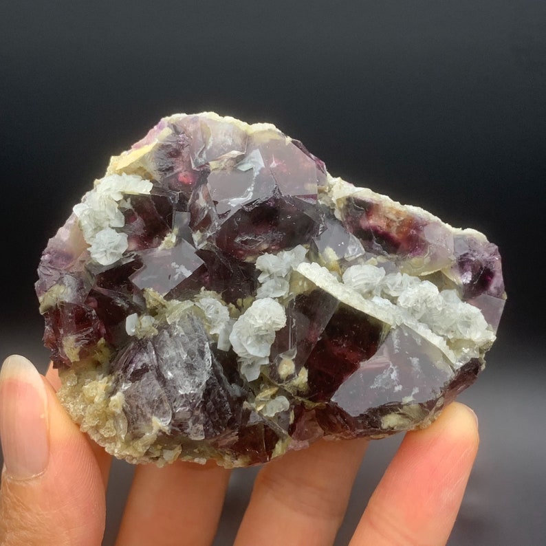 May include: A cluster of purple fluorite crystals with a green tint, set in a matrix of white calcite crystals. The fluorite crystals have a cubic shape and are translucent.