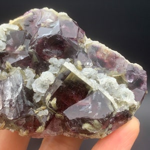 May include: A cluster of purple and green fluorite crystals with a glassy lustre. The crystals are intergrown and have a variety of shapes and sizes. Some of the crystals are partially covered in white calcite crystals.