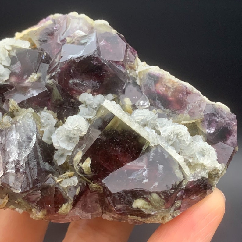 May include: A cluster of purple and green fluorite crystals with a glassy lustre. The crystals are intergrown and have a variety of shapes and sizes. Some of the crystals are partially covered in white calcite crystals.