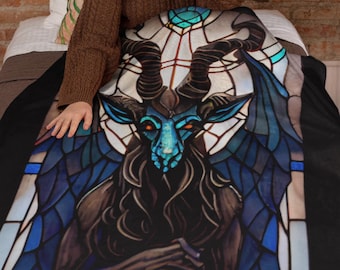 May include: A black fleece blanket with a stained glass design of a blue and black goat with horns and wings. The goat is sitting on a throne with a crown on its head.