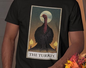 Puede incluir: Una camiseta negra con un diseño de carta de tarot vintage que presenta un pavo con la cabeza y el cuello rojos. La carta se titula "The Turkey."