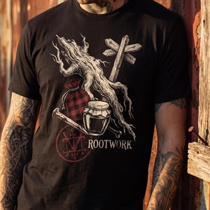 May include: A black t-shirt featuring a graphic illustration of a gnarled tree root, a wooden signpost, a red and black plaid drawstring pouch, a glass jar, a metal nail, and a red circular sigil with the text ROOTWORK printed in white.