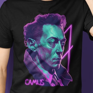Puede incluir: Una camiseta negra con un gráfico de Albert Camus en rosa y morado neón. El gráfico es un retrato estilizado de Camus con un diseño geométrico rosa y morado neón detrás de él. El texto "CAMUS" está en rosa neón debajo del gráfico.