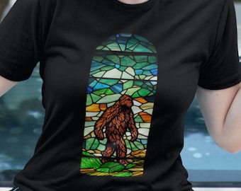 Może przedstawiać: Czarny T-shirt z witrażowym wzorem przedstawiającym Bigfoota idącego przez las. Wzór witrażowy jest w odcieniach zieleni, błękitu, żółci i pomarańczy.