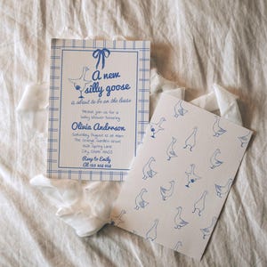 May include: Baby shower invitations in blue and white. The main invitation has a blue bow and the text: "A new silly goose is about to be on the loose." A smaller card features a pattern of blue geese.