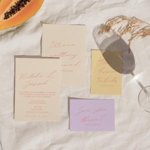 May include: Wedding invitation suite with four cards in various colors. The cards have pink script text. A slice of papaya, a glass, and a dried plant stem are also in the image. The cards read: "Natalia & Joseph", "We're getting married", "To find more details", and "See you there?"