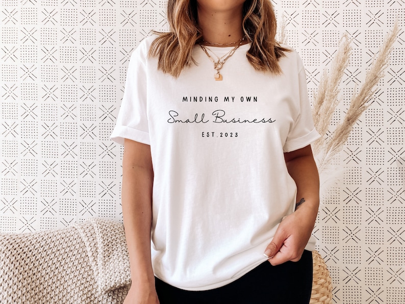 May include: White t-shirt with the text "Minding My Own Small Business Est. 2023" printed on the front.