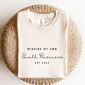May include: A white t-shirt with the text "Minding My Own Small Business Est. 2023" printed on it.