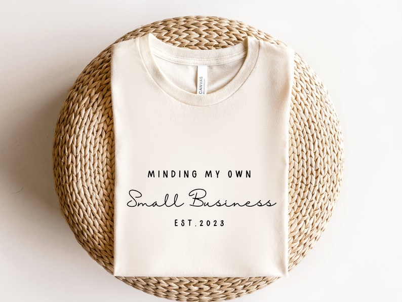 May include: A white t-shirt with the text "Minding My Own Small Business Est. 2023" printed on it.
