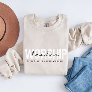 Puede incluir: Una sudadera beige con el texto "WORSHIP leader GIVING ALL I AM IN WORSHIP" impreso en la parte delantera.