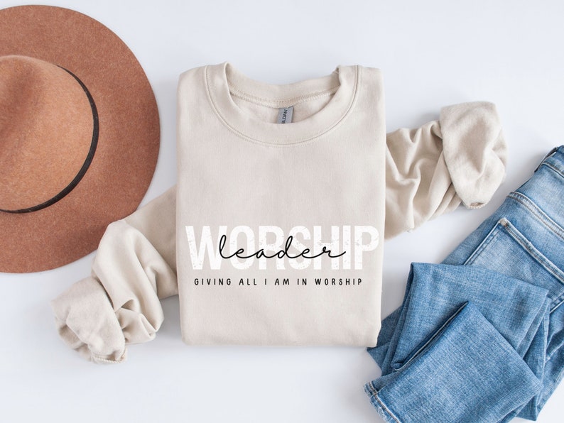 Puede incluir: Una sudadera beige con el texto "WORSHIP leader GIVING ALL I AM IN WORSHIP" impreso en la parte delantera.