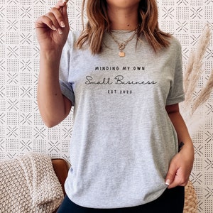 May include: A gray t-shirt with the text "Minding My Own Small Business Est. 2023" printed on the front.