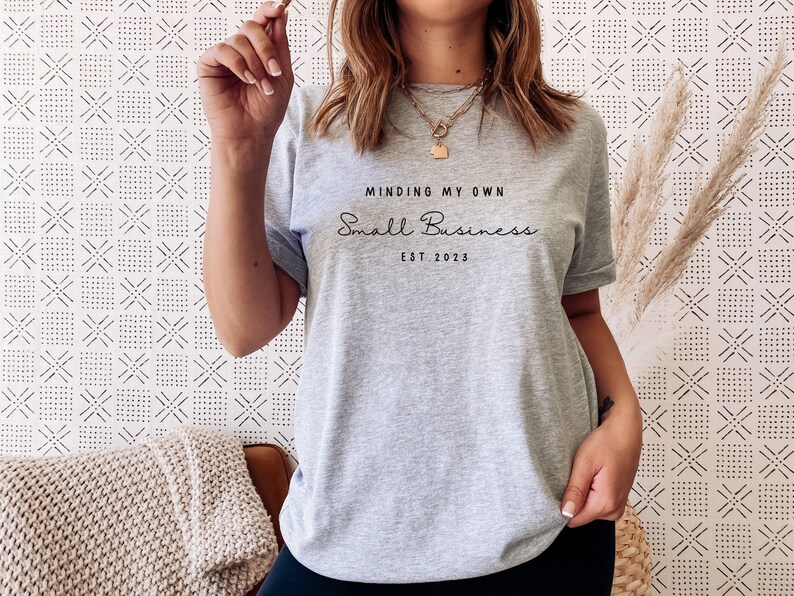 May include: A gray t-shirt with the text "Minding My Own Small Business Est. 2023" printed on the front.