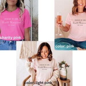 May include: Three different color variations of a pink t-shirt with the text "MINDING MY OWN Small Business EST 2023" printed on the front. The colors are charity pink, pink, and light pink.