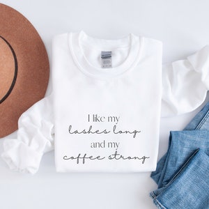 May include: White sweatshirt with the text "I like my lashes long and my coffee strong" printed on the front.