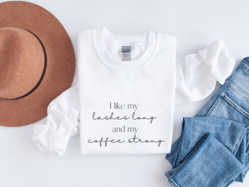 May include: White sweatshirt with the text "I like my lashes long and my coffee strong" printed on the front.