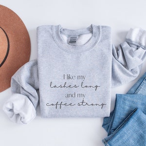 May include: Grey sweatshirt with the text "I like my lashes long and my coffee strong" printed on the front.