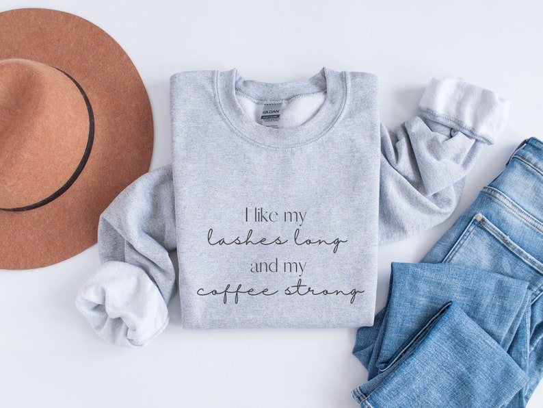May include: Grey sweatshirt with the text "I like my lashes long and my coffee strong" printed on the front.
