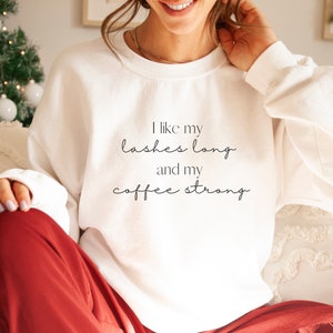 May include: White sweatshirt with the text "I like my lashes long and my coffee strong" printed on the front.