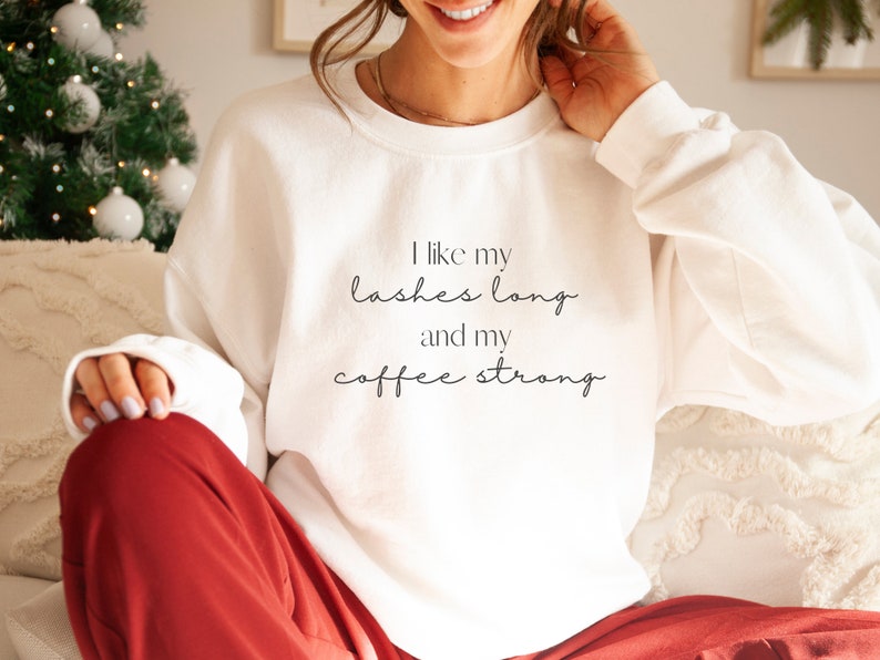 May include: White sweatshirt with the text "I like my lashes long and my coffee strong" printed on the front.