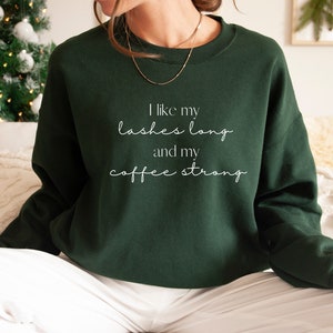 May include: A dark green sweatshirt with the text "I like my lashes long and my coffee strong" in white lettering.