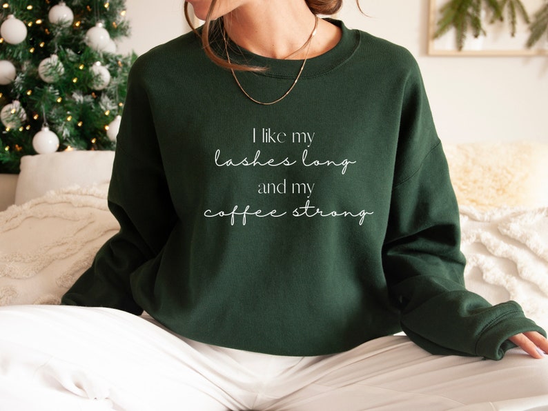 May include: A dark green sweatshirt with the text "I like my lashes long and my coffee strong" in white lettering.