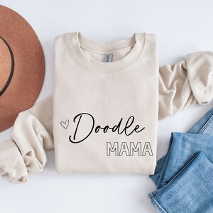 May include: A beige sweatshirt with the text "Doodle Mama" in black lettering and a small heart above the word "Doodle".