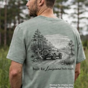 Puede incluir: Camiseta verde claro con una ilustración en blanco y negro de un Jeep en un camino de tierra con árboles. El texto "built for Louisiana back roads" está debajo. Solo una maqueta de exhibición.