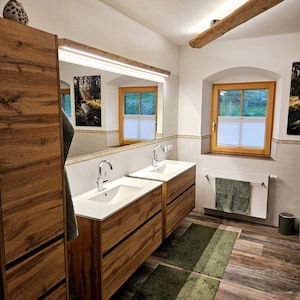 Könnte beinhalten: Modernes Badezimmer mit zwei Holzwaschtischen, jeweils mit weißem Waschbecken und Chromarmatur. Über den Waschtischen hängt ein großer Spiegel mit integrierter Beleuchtung. Der Raum hat einen Holzboden, grüne Teppiche und ein Fenster.