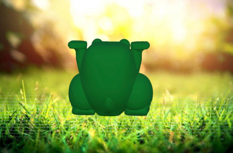 May include: A green frog figurine with a smooth, rounded surface. The frog is sitting on a bed of green grass.