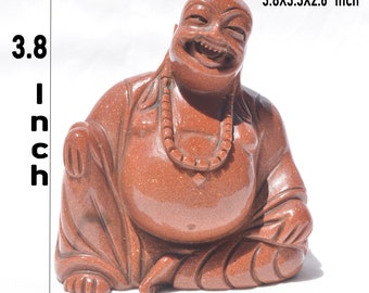 May include: A brown, sparkling sandstone Buddha figurine with a laughing expression, wearing a beaded necklace. The statue measures 3.8 inches in height, 3.3 inches in width, and 2.6 inches in depth, as indicated by the text in the image.