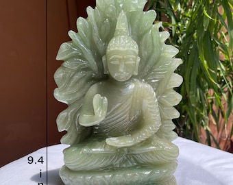 May include: A light green carved stone Buddha statue seated on a lotus base with a leaf-shaped backdrop. The figure has one hand raised in a gesture of blessing. The statue measures 9.4 inches in height and 5.8 inches in width as indicated by text.