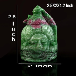 Op de afbeelding: Een groen en magentakleurig uitgesneden stenen beeldhouwwerk dat een gezicht met gesloten ogen voorstelt, met een hoogte van 7,11 cm, een breedte van 5,08 cm en een diepte van 3,05 cm. De steen vertoont natuurlijke kleurvariaties en een glad oppervlak.