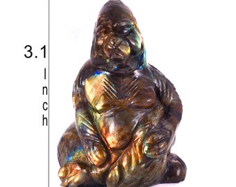 May include: A carved labradorite gorilla figurine with iridescent blue and gold flashes. The stone sculpture features a seated posture with detailed facial features and textured fur. The dimensions are clearly marked as 3.1 inches by 4.2 inches.