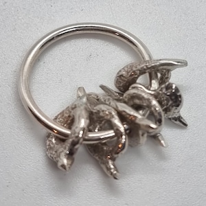 May include: A silver-toned keychain featuring a detailed, three-dimensional crab design. The crab is attached to a circular ring, creating a functional and decorative accessory. The crab's claws and body are intricately sculpted.