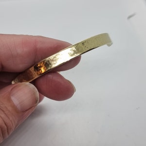 Puede incluir: Un brazalete de metal martillado dorado con un acabado liso y redondeado.