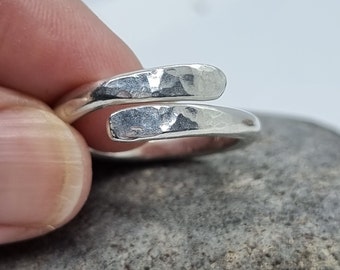 May include: A silver hammered ring with a unique twisted design. The ring is made of two pieces of metal that are twisted together to create a unique and modern look.