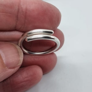 May include: A silver ring with a simple, modern design. The ring is made of two bands of metal that are twisted together.