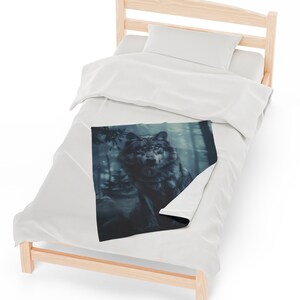 May include: A soft, blue and grey throw blanket featuring a wolf illustration in a woodland setting. The wolf is looking directly at the viewer.