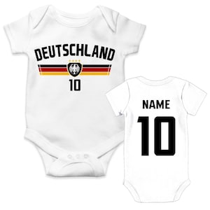 Può includere: Due body bianchi per neonati. Quello a sinistra presenta la scritta DEUTSCHLAND, una striscia orizzontale nera, rossa e oro, un emblema dell'aquila tedesca con quattro stelle e il numero 10. Quello a destra mostra la parola NAME e il numero 10.