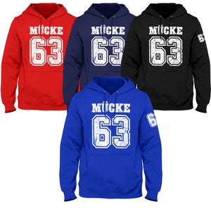 Può includere: Quattro felpe con cappuccio in diversi colori: rosso, blu navy, nero e blu royal. Ogni felpa ha una grafica bianca usurata con il nome "MÜCKE" e il numero "63" sul davanti.