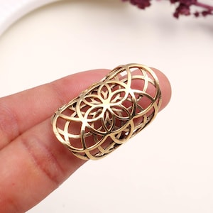Könnte beinhalten: Ein goldfarbener Ring mit einem durchbrochenen Design mit einem Blumenmuster. Der Ring ist zylindrisch und scheint aus Metall zu sein. Das filigrane Design ist vor einem neutralen Hintergrund sichtbar.