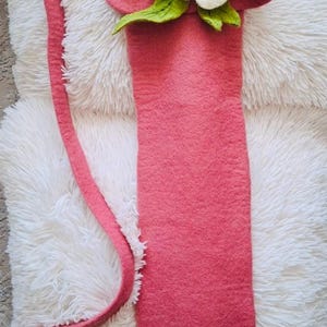 May include: A pink felt bag with a white felt flower and green felt leaves. The bag has a long strap.