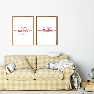 May include: Two framed prints with Christmas-themed text. The print on the left says "It's the most wonderful time of the year." The print on the right says "Have a holly jolly Christmas." The prints are hanging on a white wall above a beige sofa with a plaid pattern. A Christmas tree with brown and white baubles is in the corner of the room.