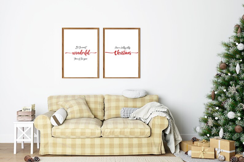 May include: Two framed prints with Christmas-themed text. The print on the left says "It's the most wonderful time of the year." The print on the right says "Have a holly jolly Christmas." The prints are hanging on a white wall above a beige sofa with a plaid pattern. A Christmas tree with brown and white baubles is in the corner of the room.