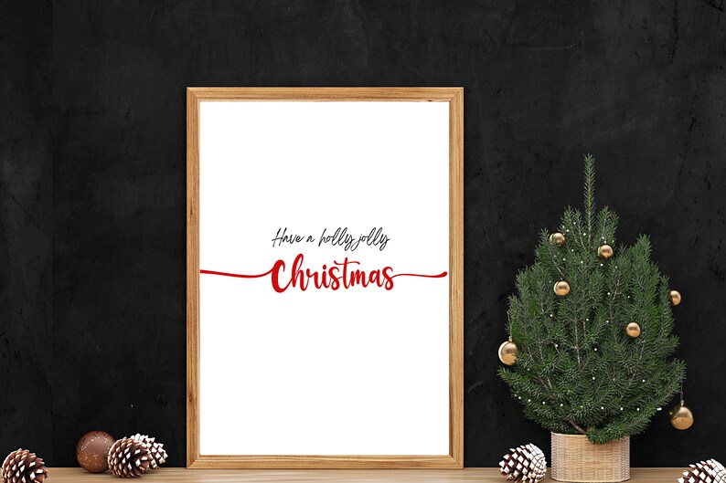 May include: A framed print with the text "Have a holly jolly Christmas" in red and black lettering on a white background. A small potted Christmas tree with gold baubles is in the foreground.