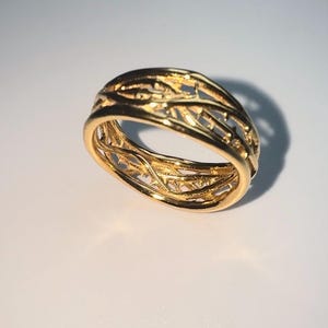 May include: A gold ring with a delicate, intricate design of interwoven branches. The ring is made of a smooth, polished metal and has a classic, timeless look.