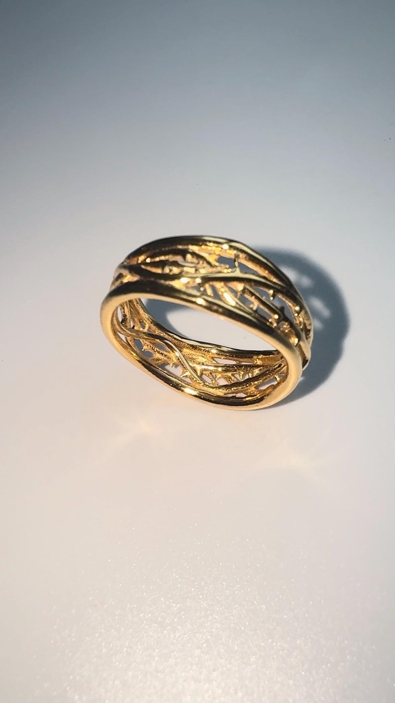 May include: A gold ring with a delicate, intricate design of interwoven branches. The ring is made of a smooth, polished metal and has a classic, timeless look.